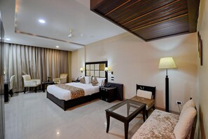 A hotel room with a large bed, a desk, a chair, a small table, and a lamp. - HOTEL FLORET INN (Durg)