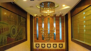 A spacious lobby with a high ceiling, a chandelier, a large wall clock, and a seating area. - HOTEL FLORET INN (Durg)