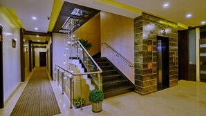 A modern hotel lobby with a glass staircase, a reception desk, and a wall-mounted elevator. - HOTEL FLORET INN (Durg)