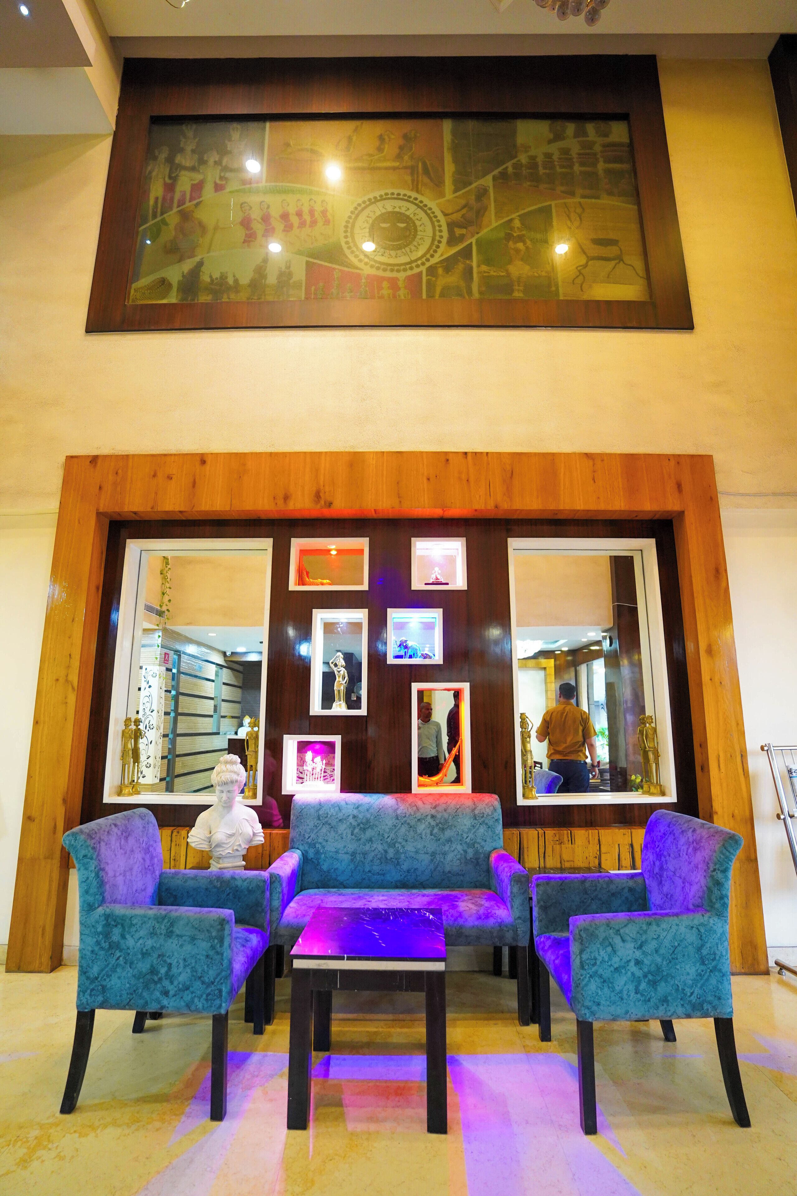 A lobby with a wooden reception desk, blue velvet chairs, and a large mirror reflecting the interior.