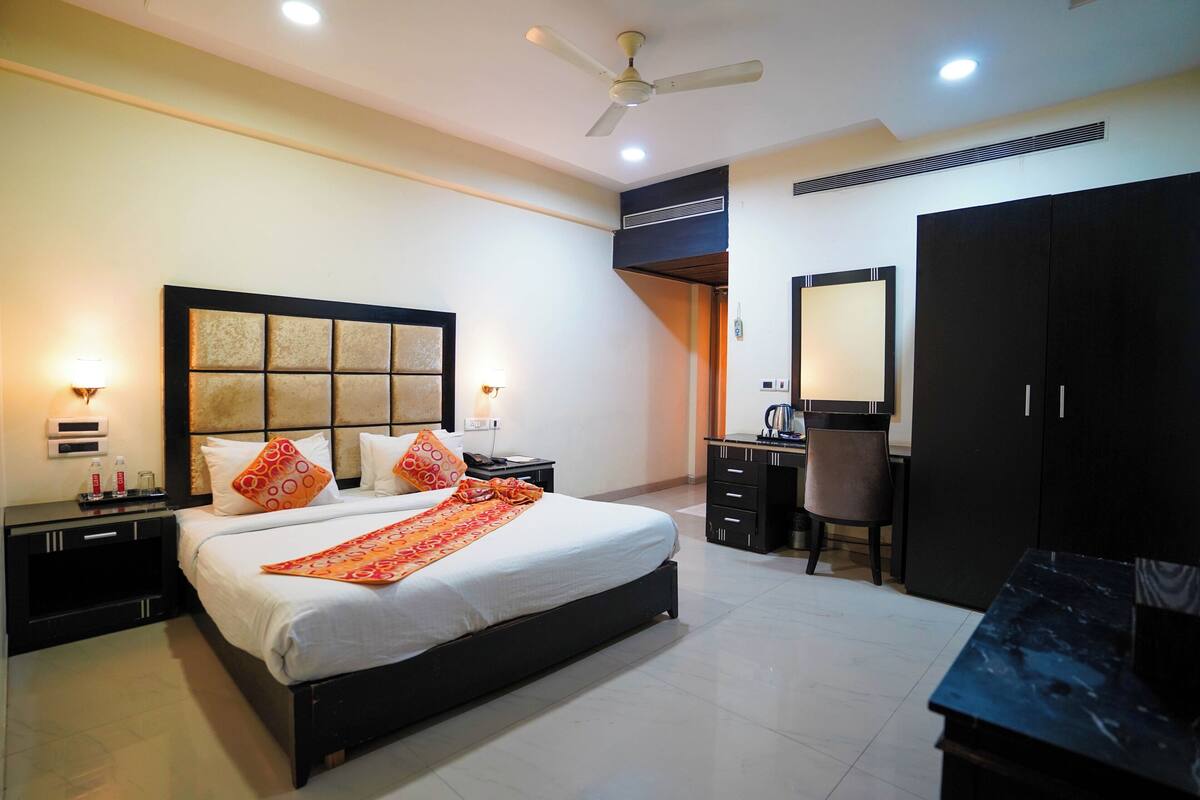 A hotel room with a large bed, a desk with a chair, a wardrobe, and a ceiling fan.
