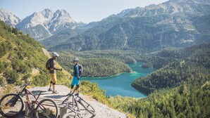 En mountainbikeled med två cyklister och en cykel, omgiven av skogbeklädda berg och en sjö.