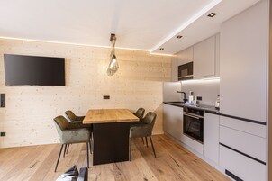 A modern kitchen with a wooden dining table, grey upholstered chairs, and built-in appliances.