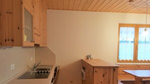 A kitchen with wooden cabinets, a sink, a stove, and a window with curtains. - Bright Apartment Near Thermal Springs (Bad Kleinkirchheim)