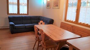 A cozy room with a wooden table and chairs, a dark blue sofa, and a window with lace curtains. - Bright Apartment Near Thermal Springs (Bad Kleinkirchheim)