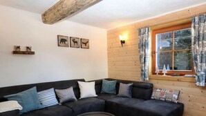 A cozy living room with a sectional sofa, a round coffee table, and a wooden ceiling beam. There are three wall-mounted animal pictures and a window with curtains. - Apartment in Ebene Reichenau With Garden (Reichenau)