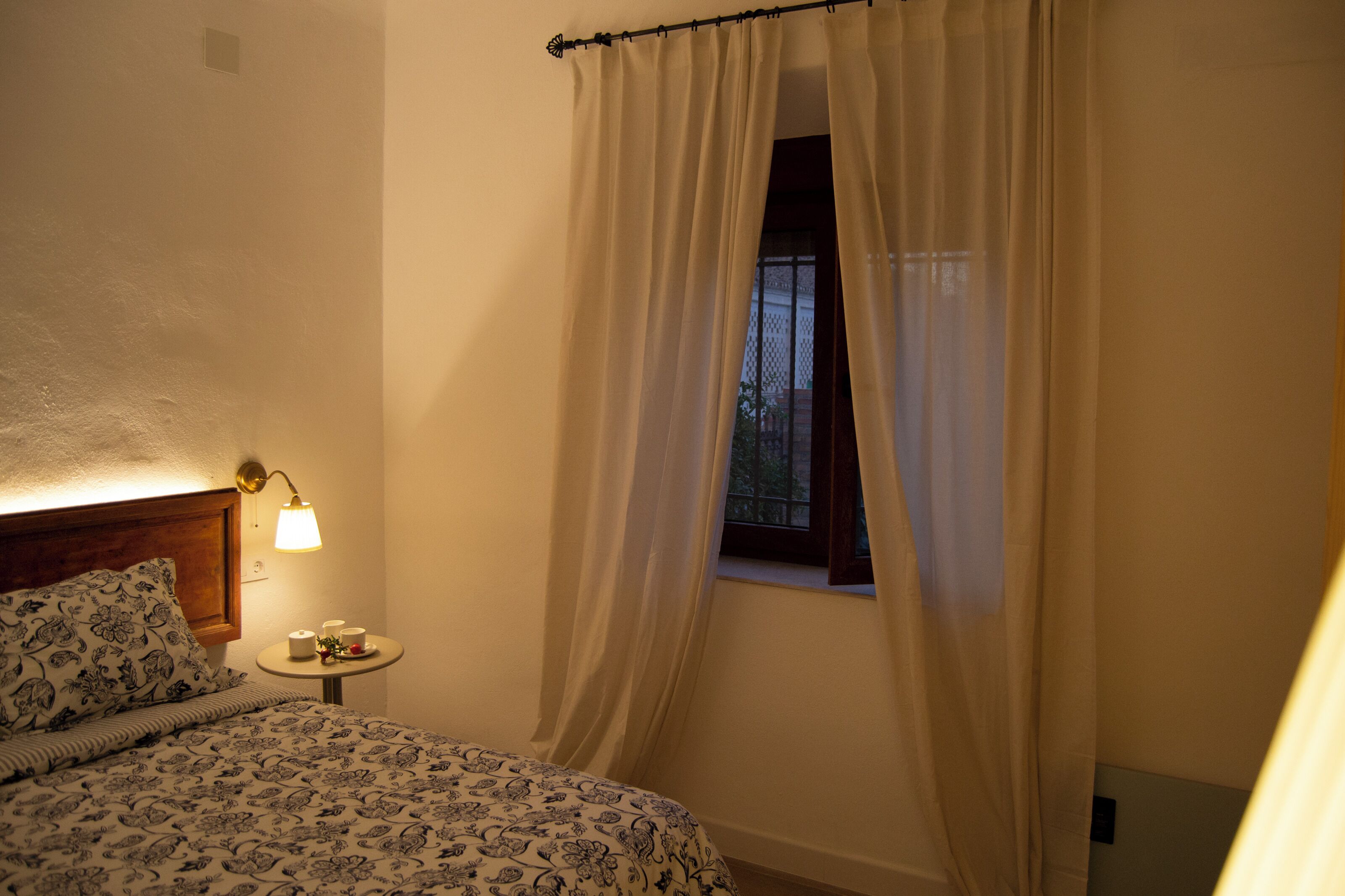 Ein Schlafzimmer mit einem Bett, einem Nachttisch mit Lampe und einem Fenster mit Vorhängen.