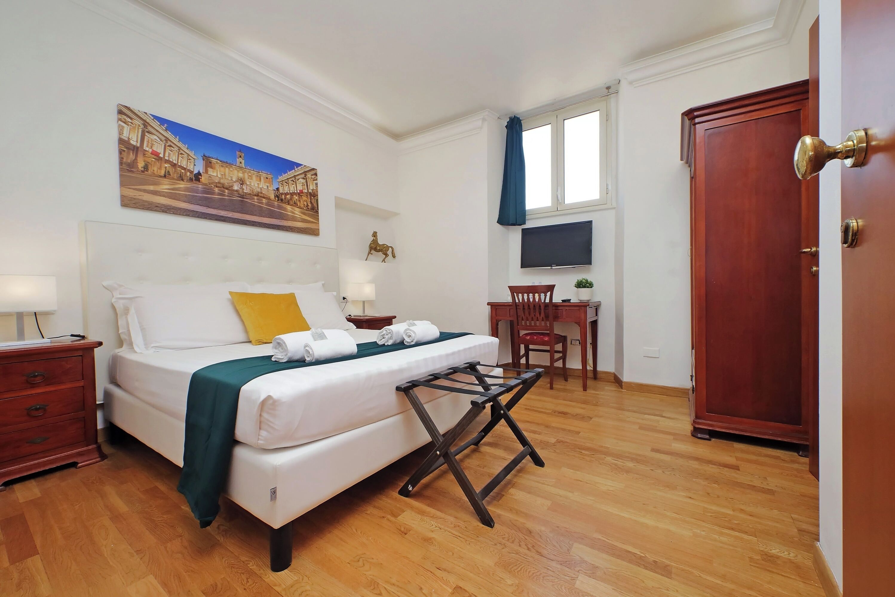 Una habitació d'hotel amb un llit, una taula de treball, una cadira, un televisor i una porta.