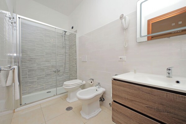A modern bathroom with a glass-enclosed shower, a toilet, a bidet, and a vanity with a mirror. - Romulus Rooms (Rome)