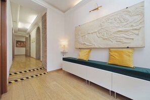Un couloir doté d’un plancher en bois, d’un banc avec des coussins jaunes et d’une grande fresque murale.