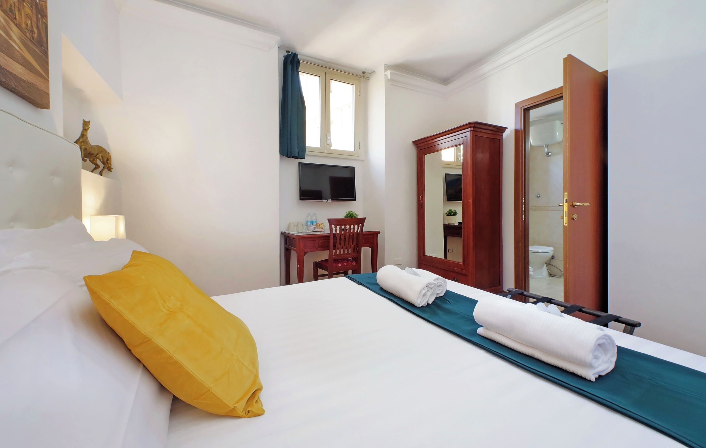 A hotel room with a bed, a desk, a chair, a TV, a mirror, and a bathroom door.