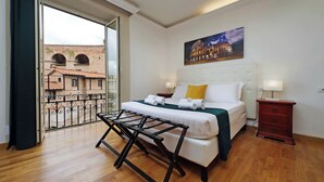 Ein Hotelzimmer mit Bett, Nachttisch, Lampe und einem Balkon mit Blick auf ein historisches Gebäude.