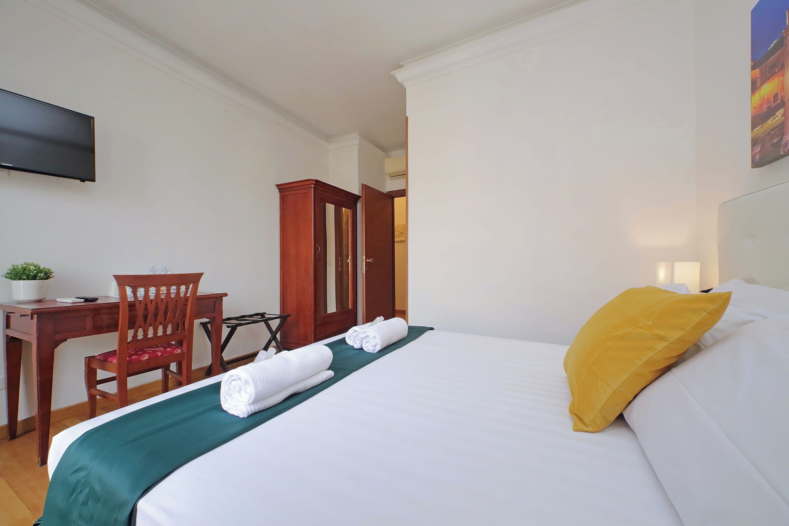 A hotel room with a bed, a desk, a chair, and a television on the wall.