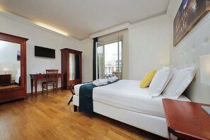 Une chambre d’hôtel équipée d’un lit, d’un bureau, d’une chaise, d’une télévision et d’une fenêtre donnant sur des immeubles.