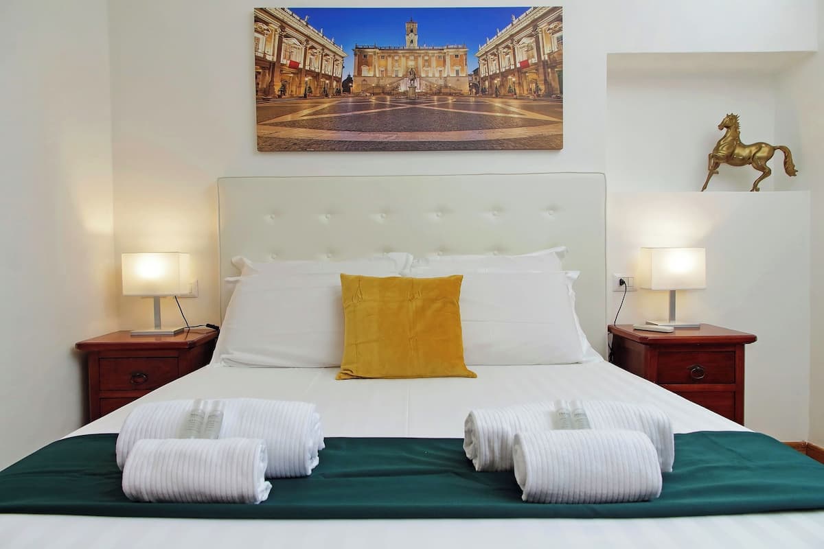 A hotel room with a large bed, white bedding, a green throw, and two nightstands with lamps.