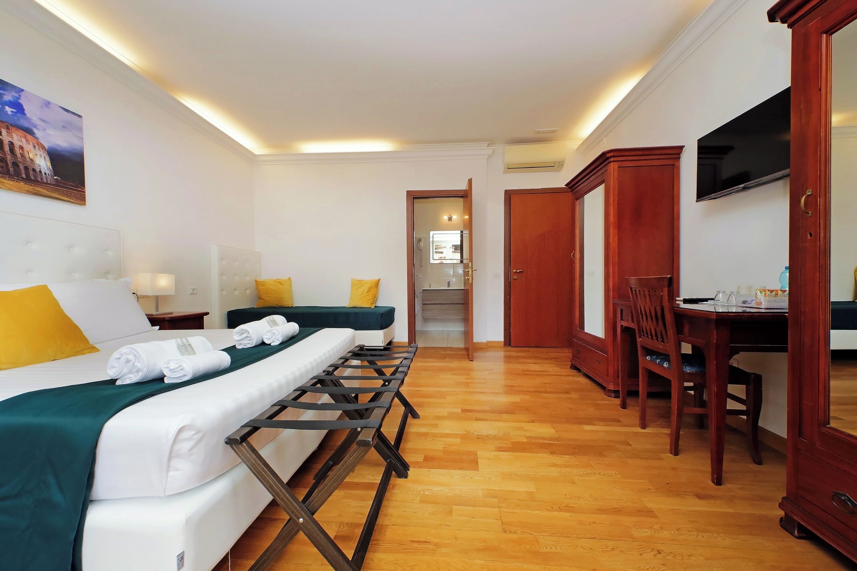 Habitación de hotel con cama, escritorio y silla. Hay un cuadro en la pared y un televisor montado allí.