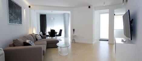A modern living room with a sofa, a glass coffee table, and a flat-screen TV.