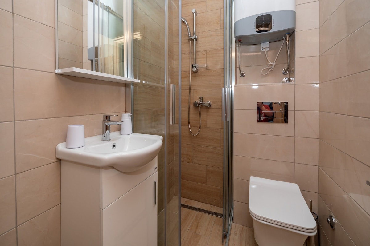 Un baño moderno con ducha de vidrio, lavamanos blanco y retrete.