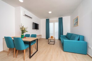 A modern living room with teal furniture, a dining area, and a flat-screen TV mounted on the wall. - Apartments Bonazza (Petrovac)