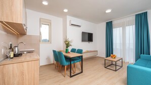 Una sala de estar moderna con sofá, una mesa de comedor con sillas, una zona de cocina con lavaplatos y un televisor de pantalla plana montado en la pared.