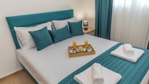 Una cama bien hecha con ropa de cama color turquesa, una bandeja con alimentos para el desayuno y una toalla doblada sobre la cama.
