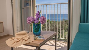 Un balcón con vista al mar, un florero con flores, un libro y un lazo sobre una mesa.
