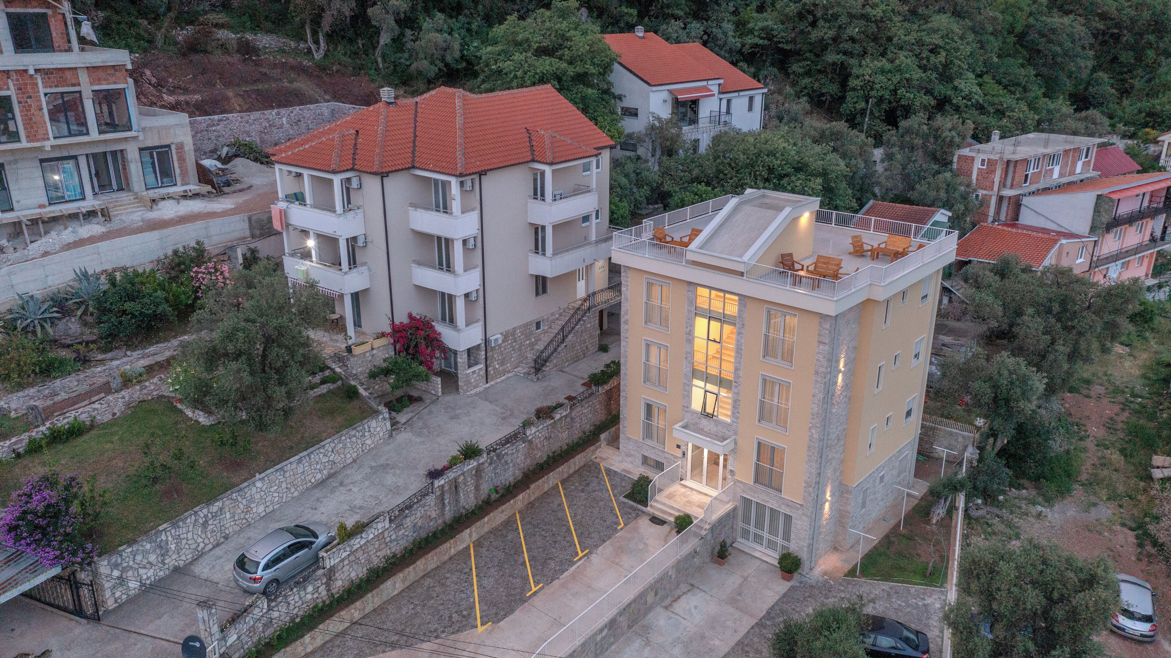 A multi-story residential building with balconies, a parking area, and surrounding greenery.