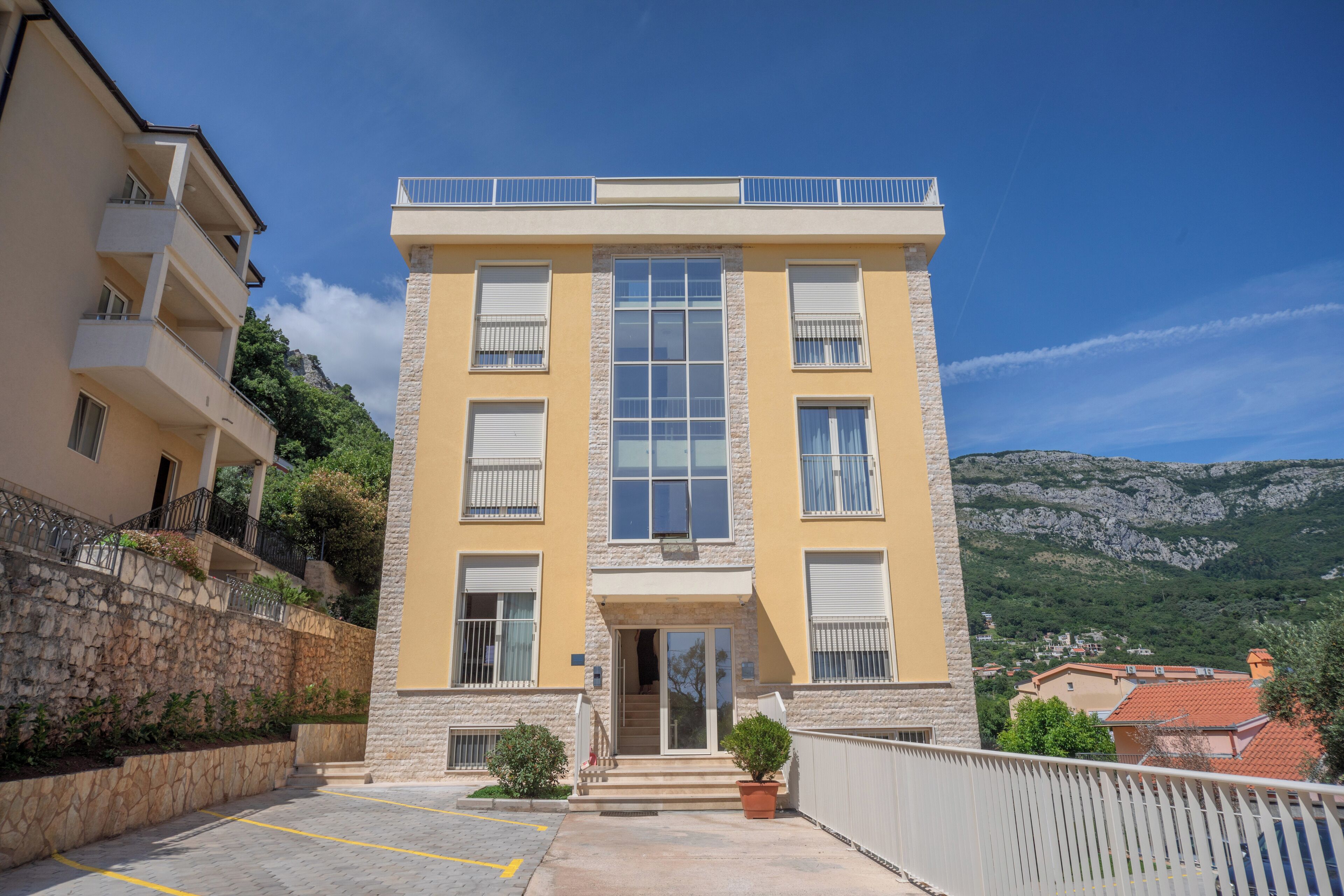 Un immeuble à plusieurs étages doté d’une entrée centrale, de balcons et d’un mur de soutènement en pierre.
