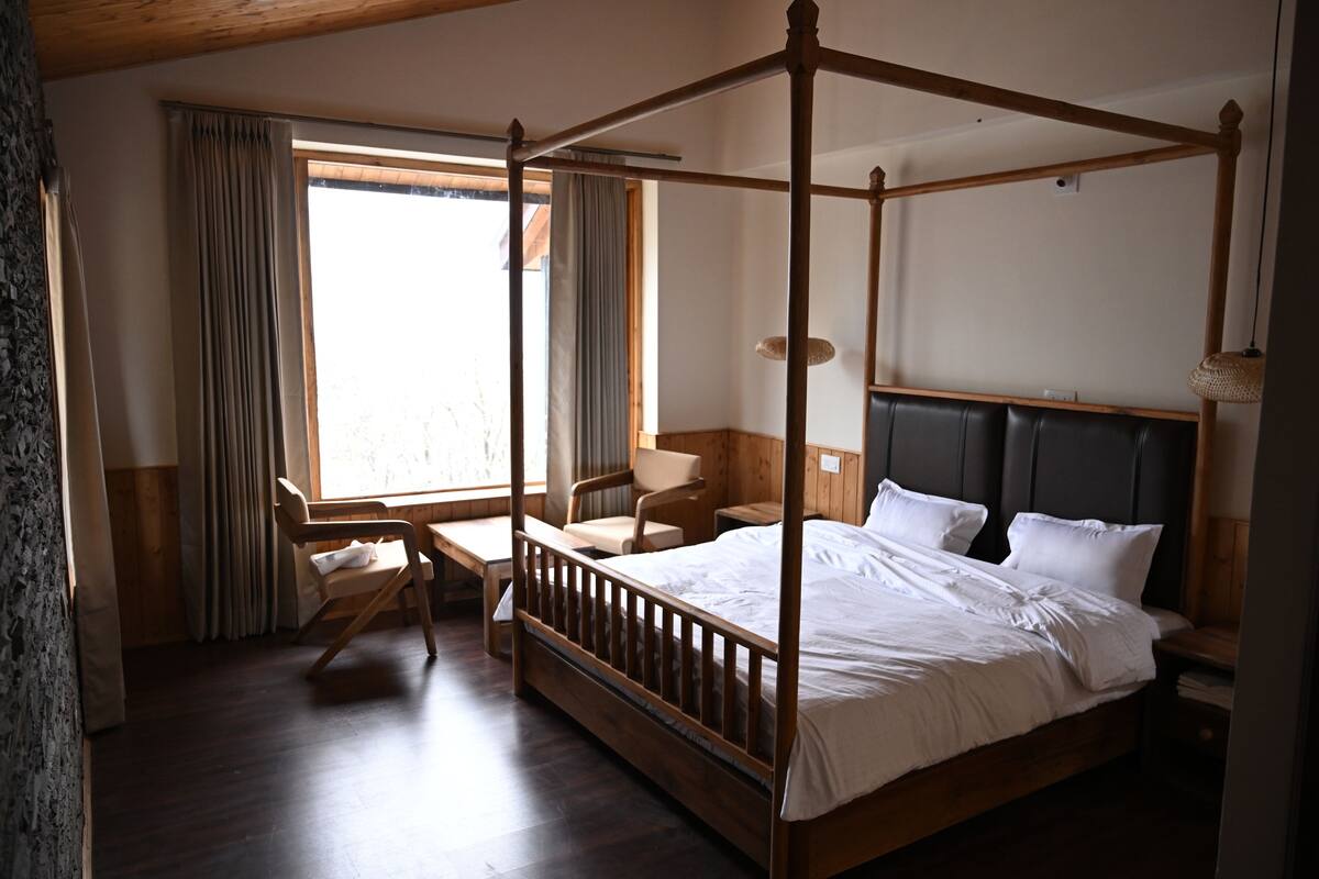 A four-poster bed with a headboard, a desk with a chair, and a window with curtains.