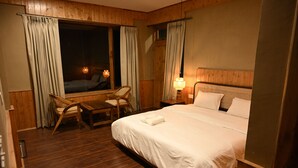 Una habitación de hotel con una cama grande, un cabecero de madera, una ventana con cortinas, un escritorio con una silla y dos lámparas de noche.