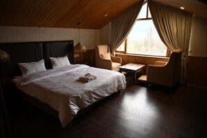 A bedroom with a large bed, a small desk, a chair, and a window with curtains.