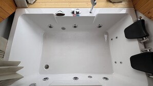 Una bañera blanca con ducha, múltiples grifos y un panel de control.