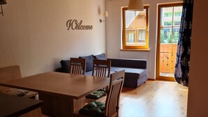 Une table à manger en bois avec des chaises, un canapé et une pancarte « Bienvenue » accrochée au mur.