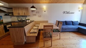 Une cuisine moderne avec des meubles en bois et un îlot central, un coin repas avec une table et des chaises en bois, et un canapé bleu dans l’espace salon.