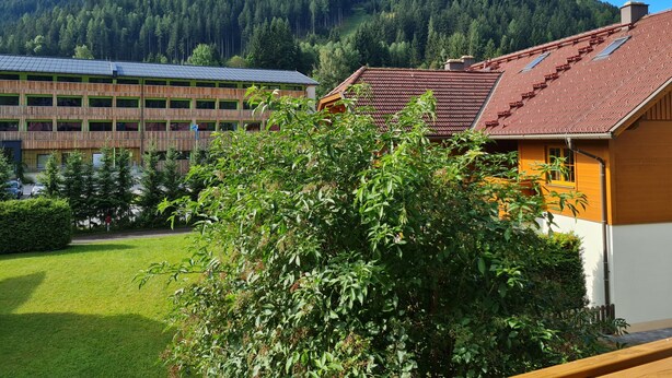 Un bâtiment coiffé d’un toit de tuiles rouges, entouré de verdure et avec une montagne en arrière-plan.