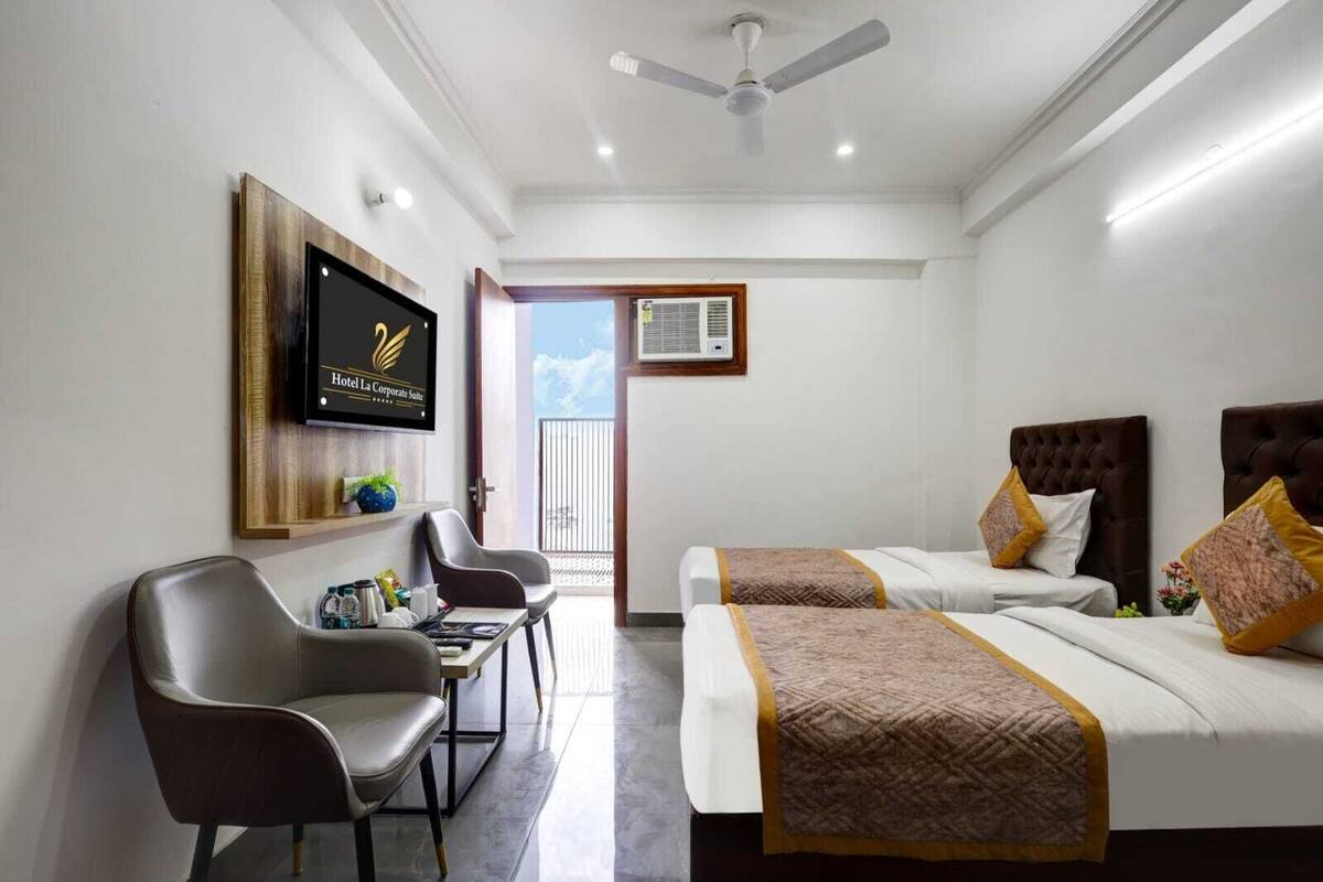A hotel room with two beds, a desk, a chair, a TV, and a balcony with a view.