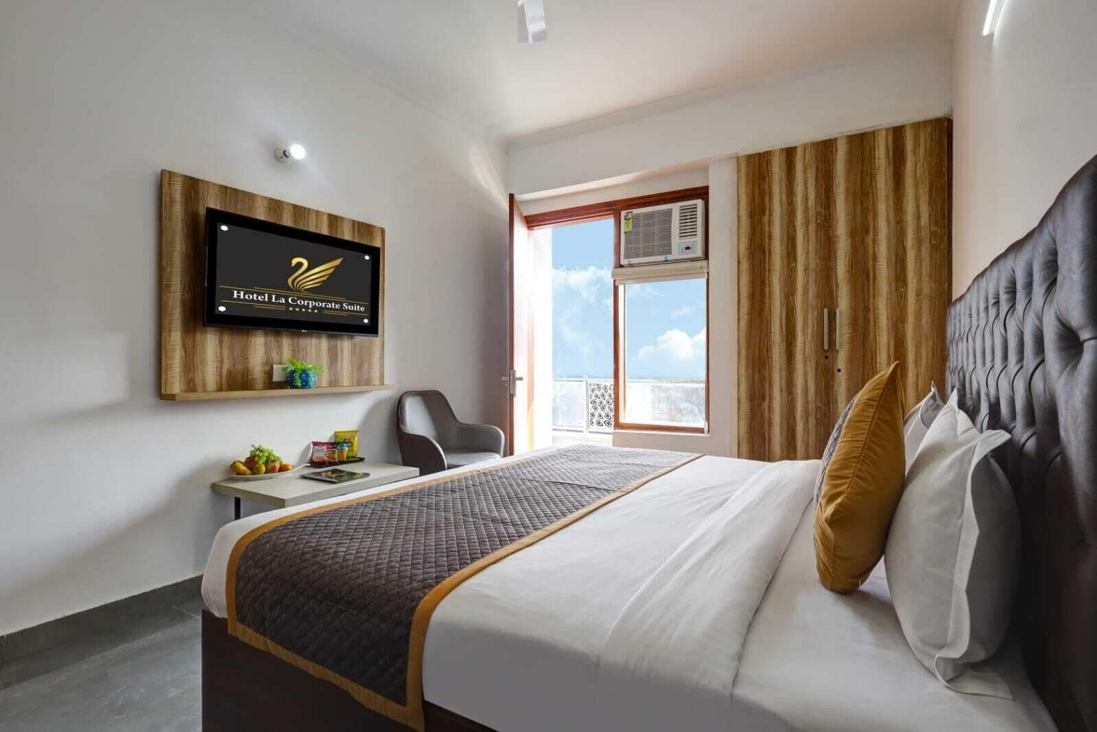 Habitación de hotel con cama, escritorio, silla, televisión montada en la pared y ventana con cortinas.