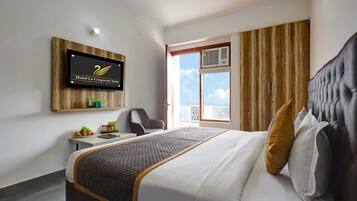 Habitación de hotel con cama, escritorio, silla, televisión montada en la pared y ventana con cortinas.