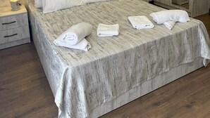 A neatly made bed with white linens and towels, a wooden wardrobe, and a nightstand with a lamp.