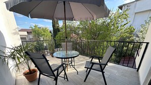 A balcony with a round glass table and two chairs, a large umbrella, and potted plants.