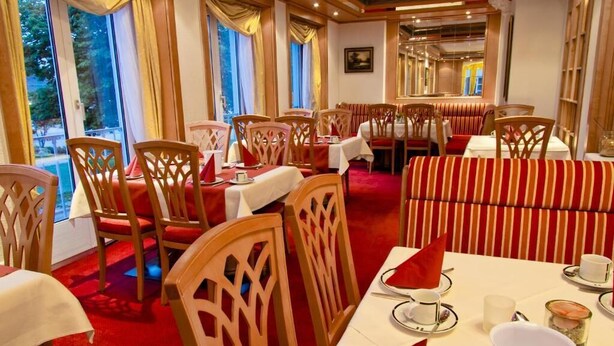 Un restaurante con sillas y mesas de madera, asientos con boiserie a rayas rojas y blancas, y amplias ventanas con cortinas.