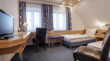 A compact hotel room with a desk, a bed, a chair, and a television.