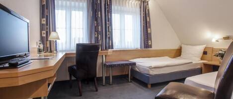 A compact hotel room with a desk, a bed, a chair, and a television.
