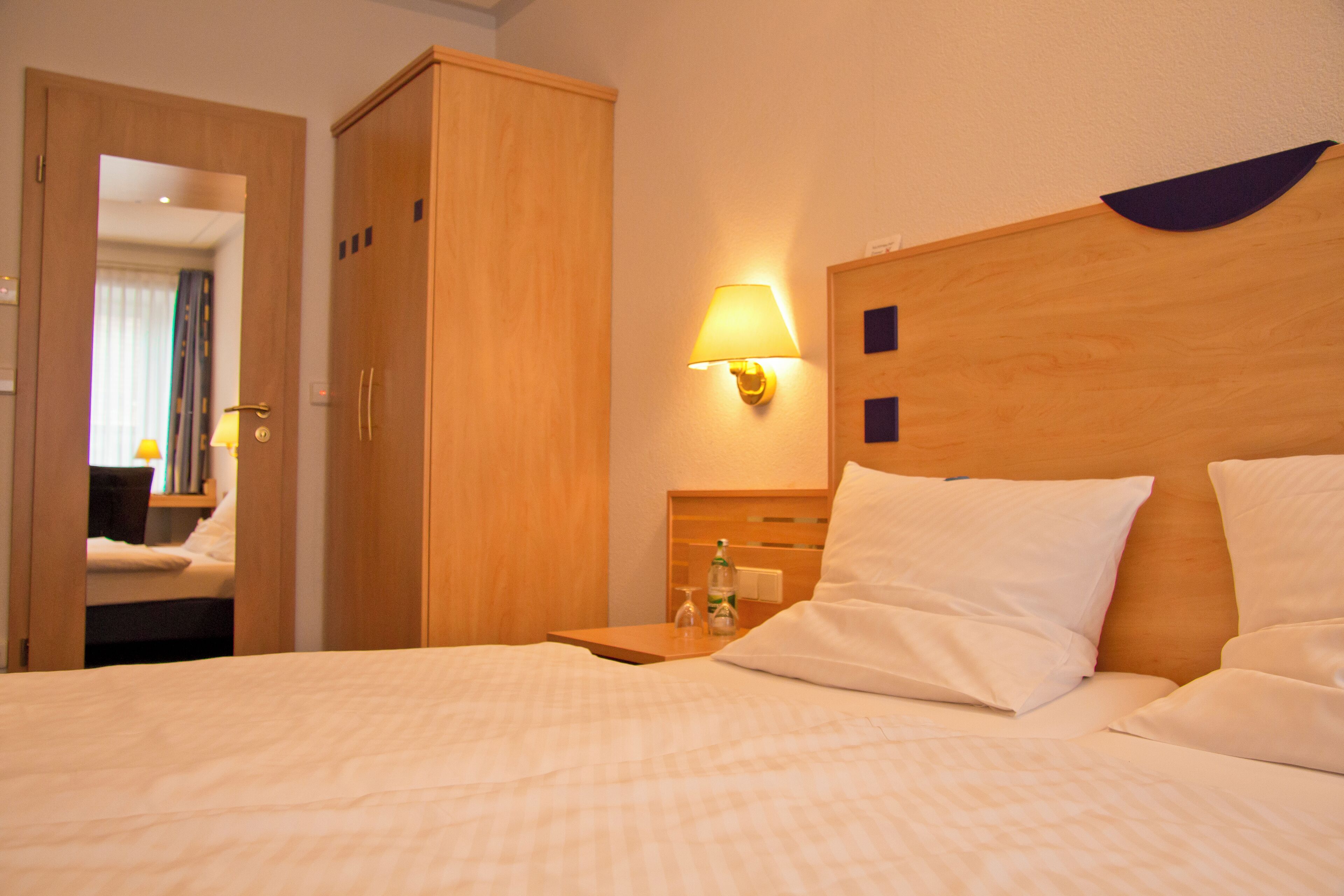 Una habitación de hotel con cama, armario, mesita de noche con lámpara y espejo.