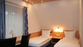 A hotel room with two single beds, a desk with a chair, and a window with curtains.