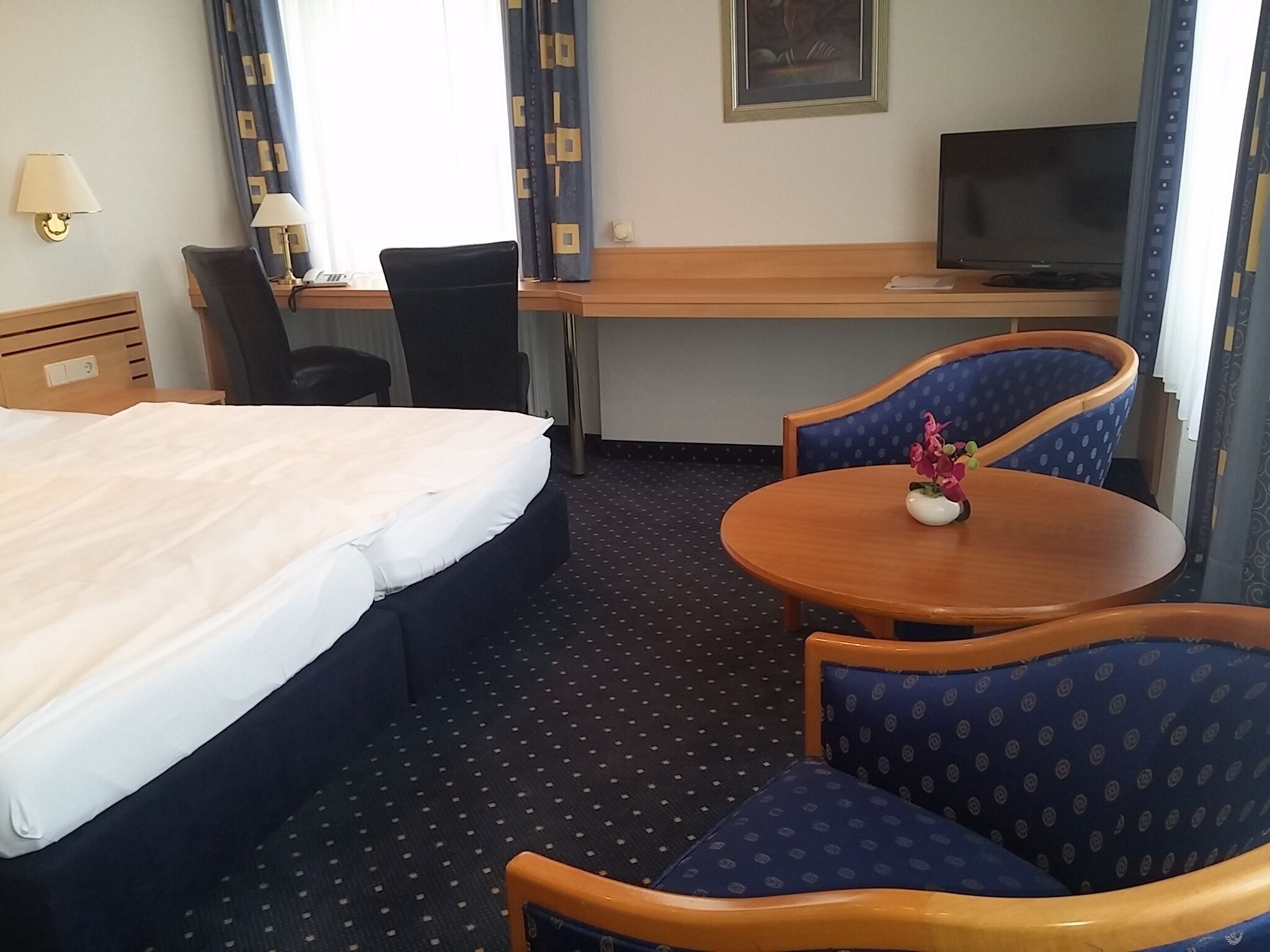 Ein Hotelzimmer mit Bett, Schreibtisch, Fernseher und zwei Stühlen.