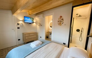 Habitación de hotel con cama, televisor montado en la pared, cómoda de madera, baño con ducha y un adorno en la pared.