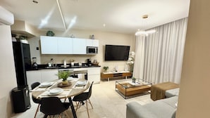 Una sala moderna con un sofá gris, una mesa de centro y un comedor con una mesa dispuesta para cuatro.