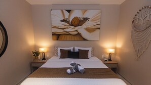 Una habitación de hotel con una cama grande, dos mesitas de noche con lámparas, una obra de arte floral en la pared y un tapiz de macramé.
