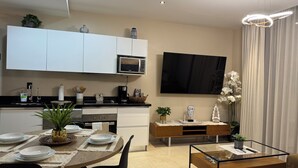 Cocina moderna con alacenas blancas, microondas y comedor con mesa de madera para cuatro.